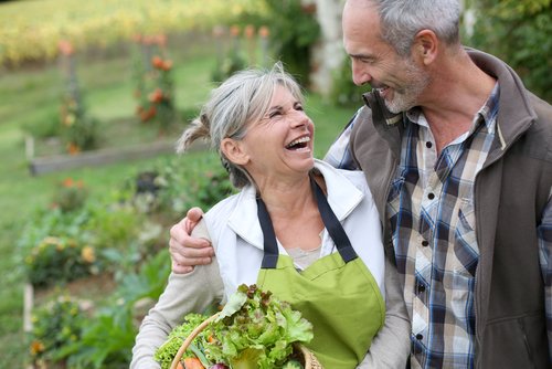 Gray-haired couple smile at each other in a vegetable garden